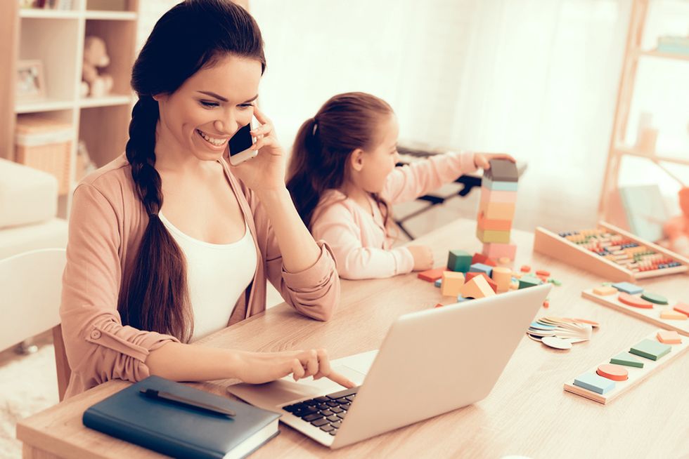 A busy mother works a stay-at-home job while taking care of her daughter.
