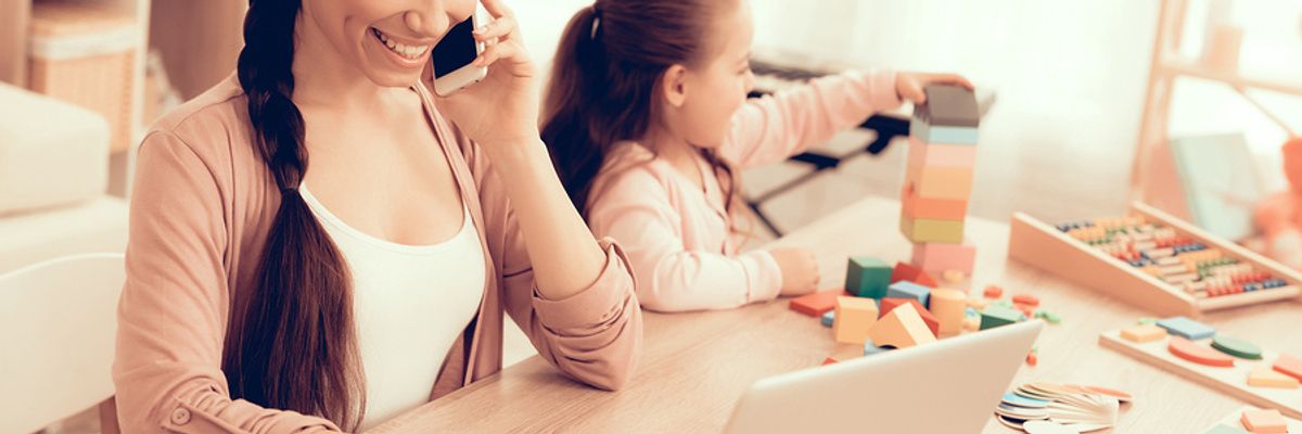 A busy mother works a stay-at-home job while taking care of her daughter.