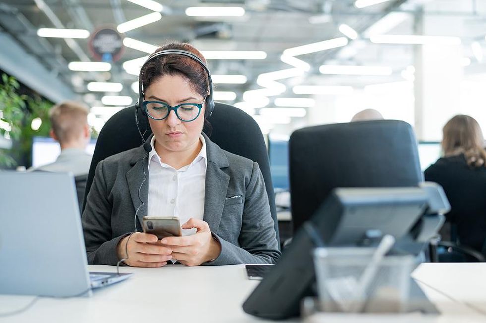 A distracted employees searches on her phone for a new job while at work.