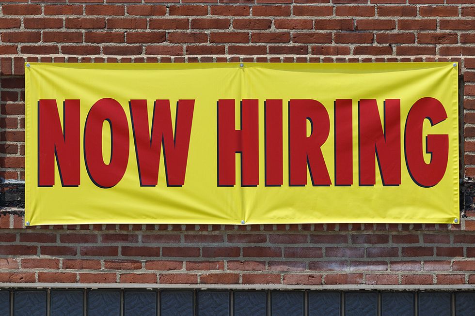A now hiring sign hangs above a storefront.