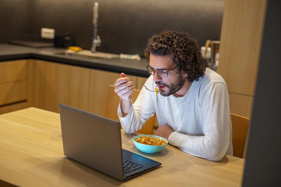 A remote worker eats dinner as he continues to work.