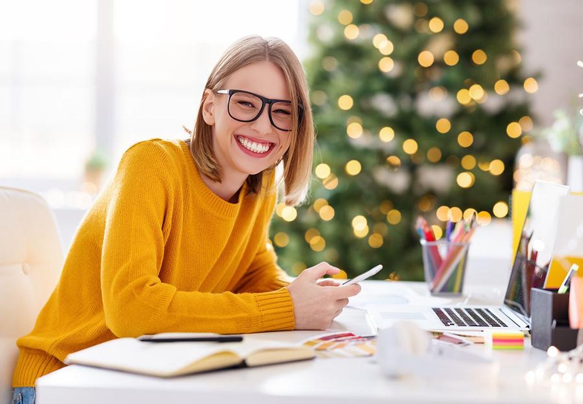 A smiling remote worker has a Christmas tree in her home office