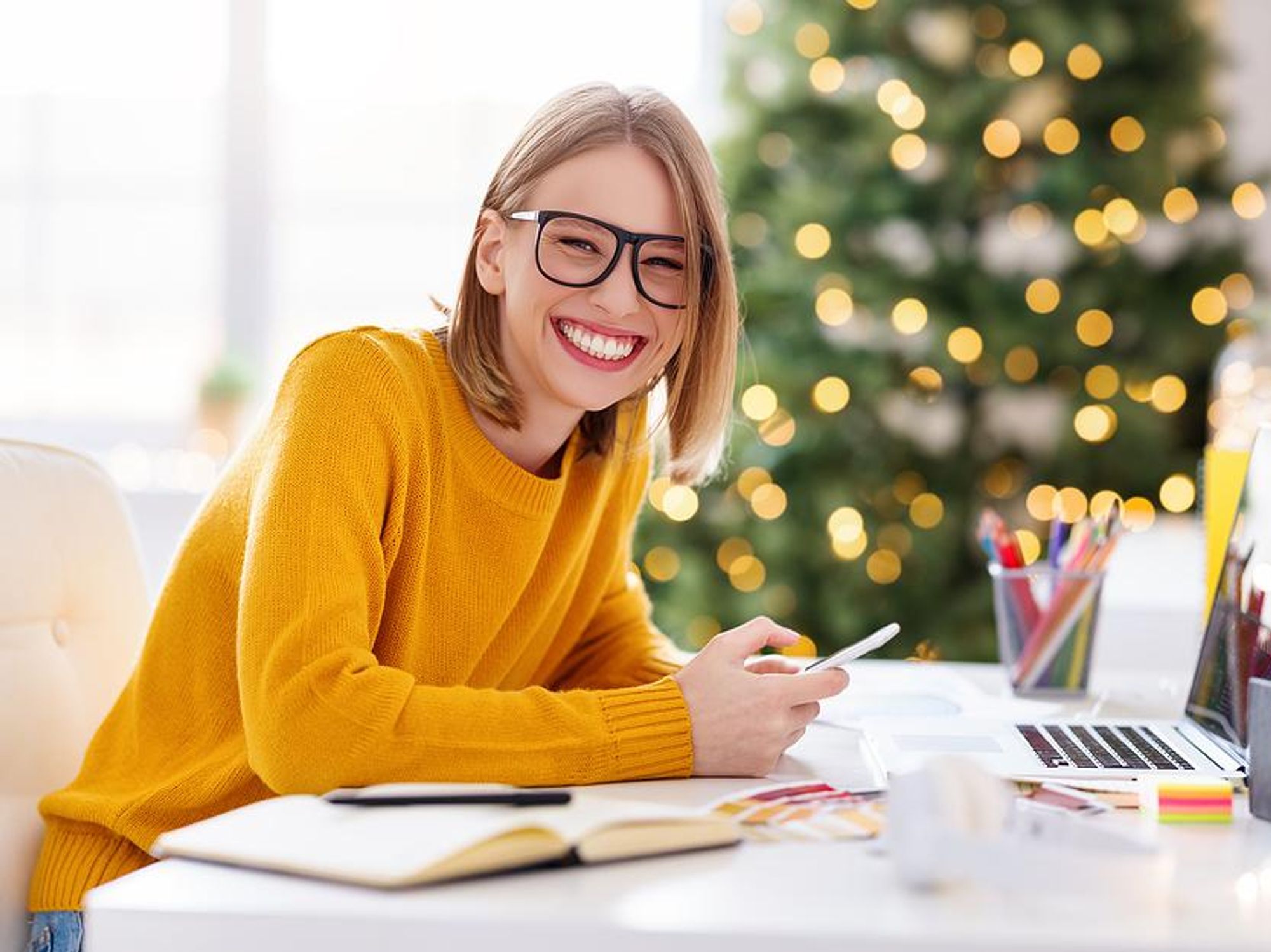 A smiling remote worker has a Christmas tree in her home office