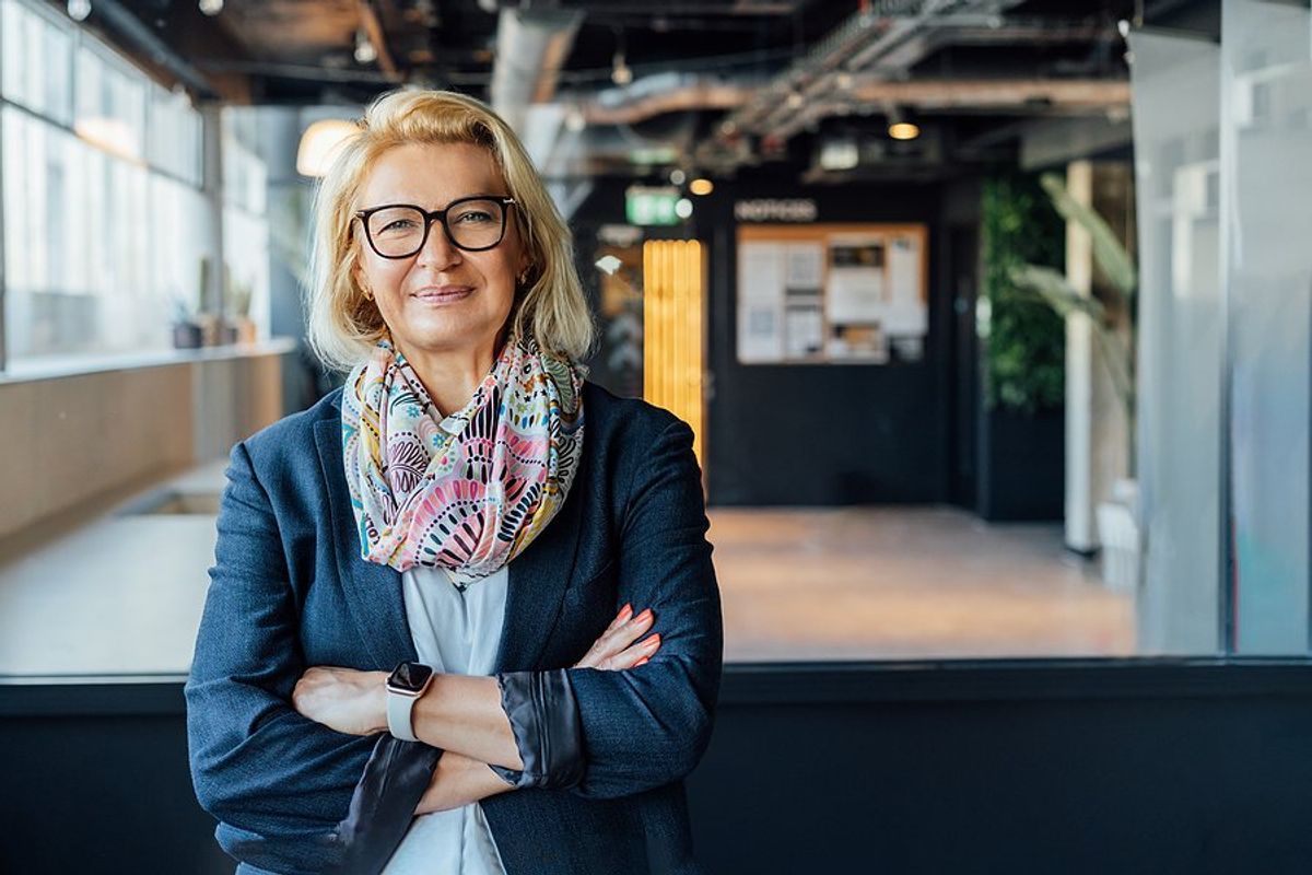 CEO/leader/executive smiles and stands with her arms crossed while thinking about people vs. profit