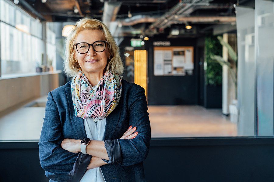 CEO/leader/executive smiles and stands with her arms crossed while thinking about people vs. profit