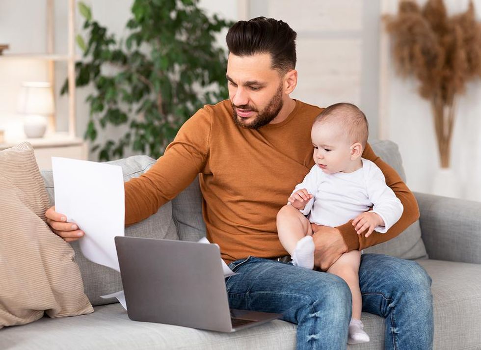 Dad holds his baby while working from home