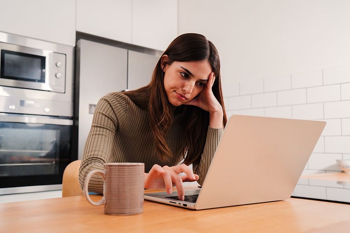 Frustrated/bored woman on laptop feels bad for being unproductive in her job