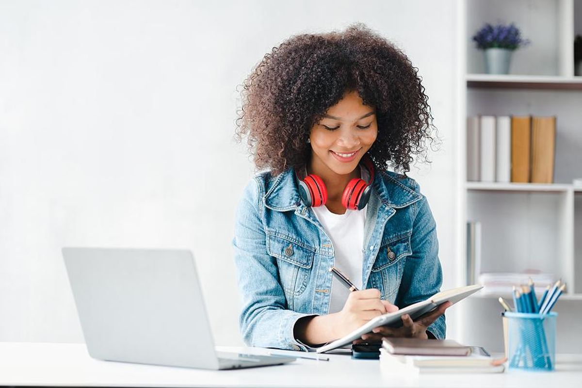 Gen Zer/young professional/college student writes something down while using her laptop