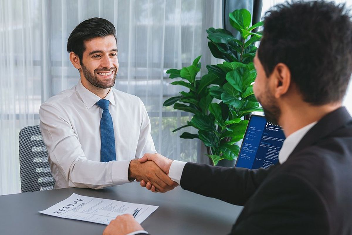 Happy job candidate shakes hands with the hiring manager in an interview before answering, "Why should we hire you?"