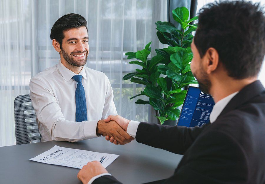 Happy job candidate shakes hands with the hiring manager in an interview before answering, "Why should we hire you?"