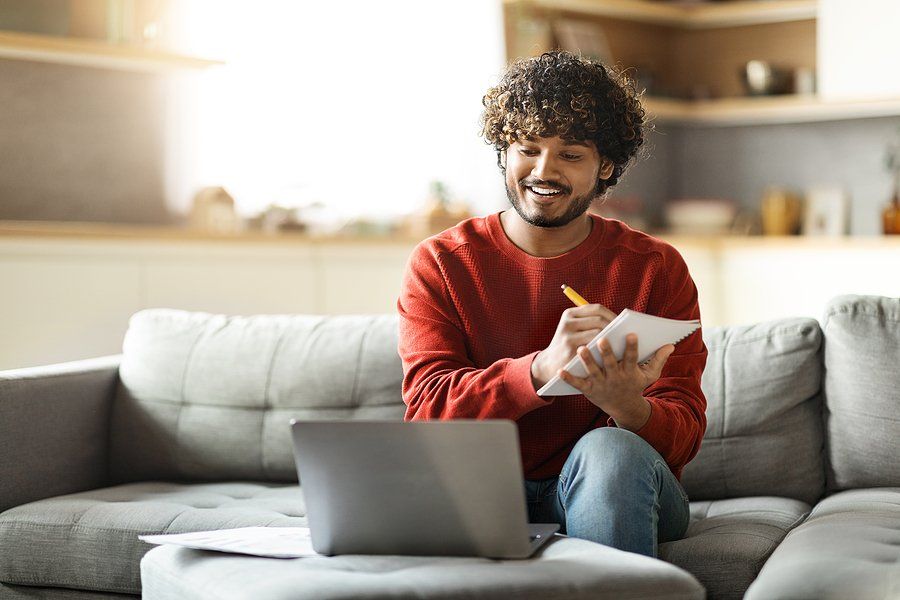 Happy man on laptop writes something down while conducting a stealth job search