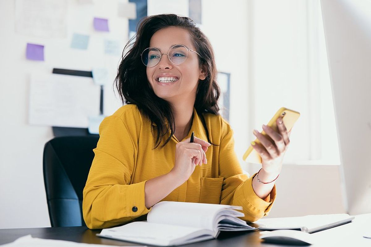 Happy woman at work holds phone while she takes notes
