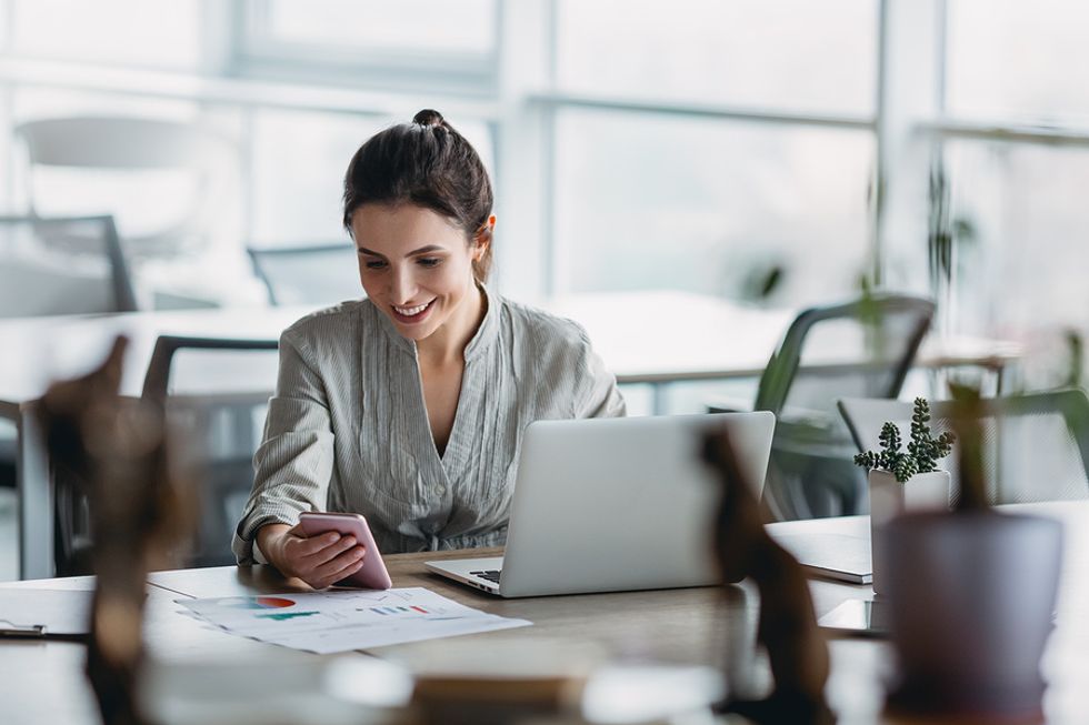 Happy woman checks her phone while writing a cover letter