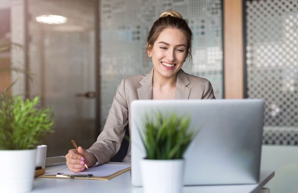 Happy young businesswoman on laptop getting set up for work on her first day in a new office