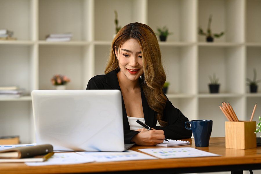 Happy young professional woman looking at laptop and taking notes on job trends