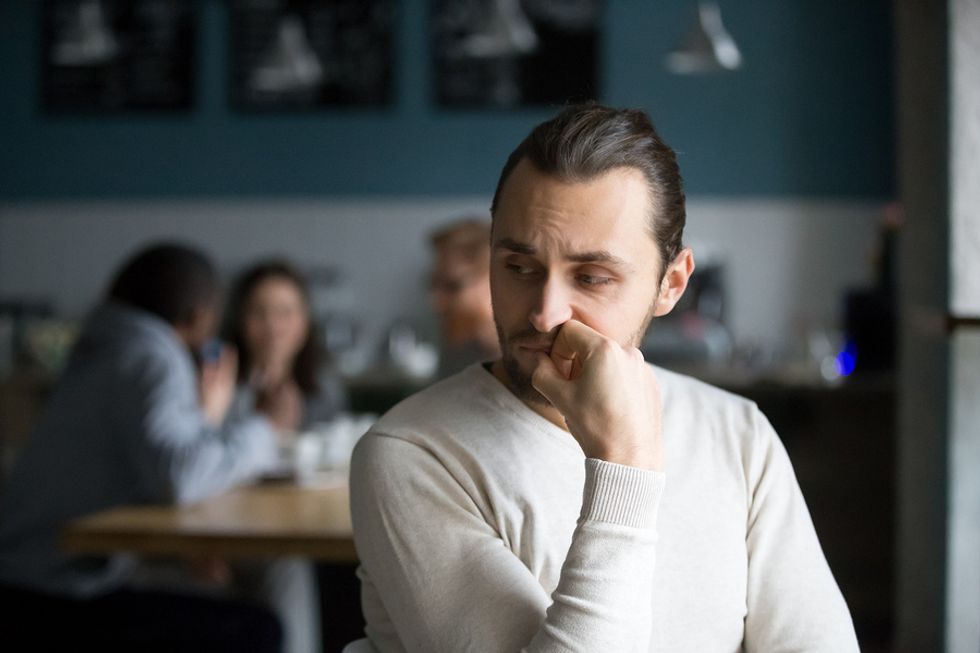 Introverted young man sitting separate from his coworkers in a break room.