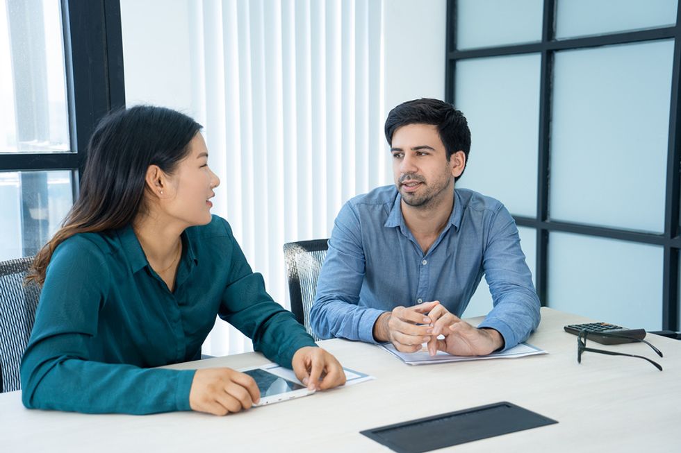 Male and female co-workers sitting next to one another at a desk, sharing why they think their relationship as co-workers is difficult.