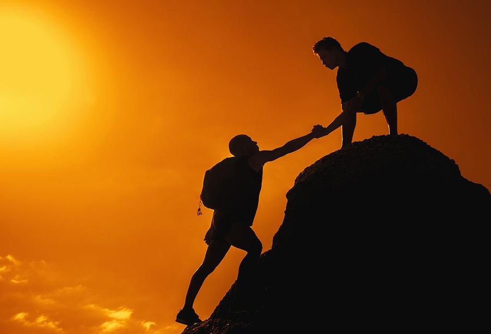 Man helps his friend climb a mountian