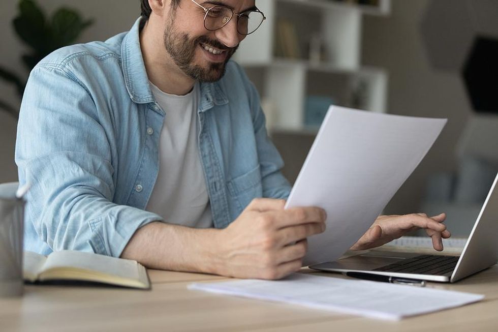 Man holds his resume while working on laptop