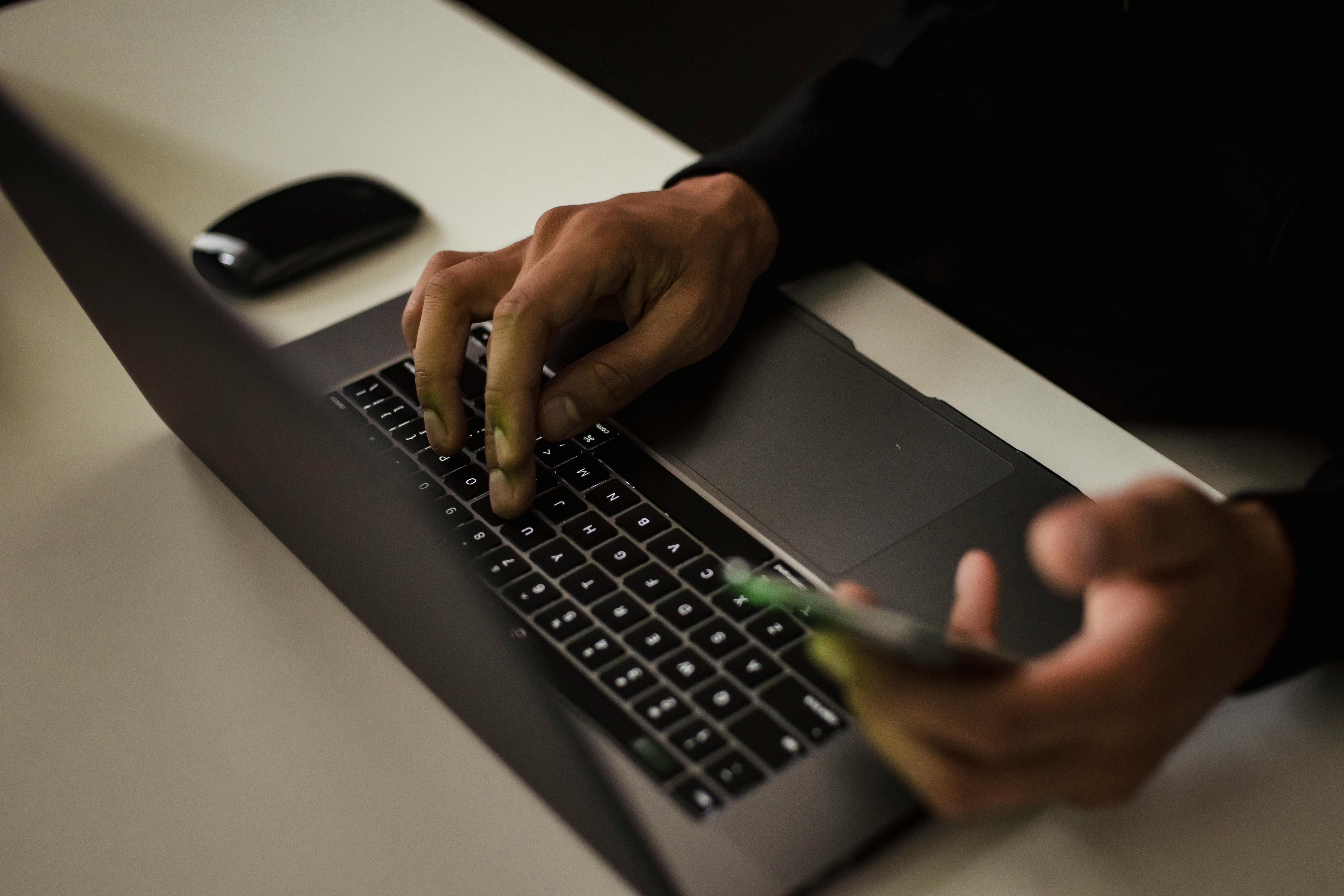 Man holds phone while typing an email on his laptop