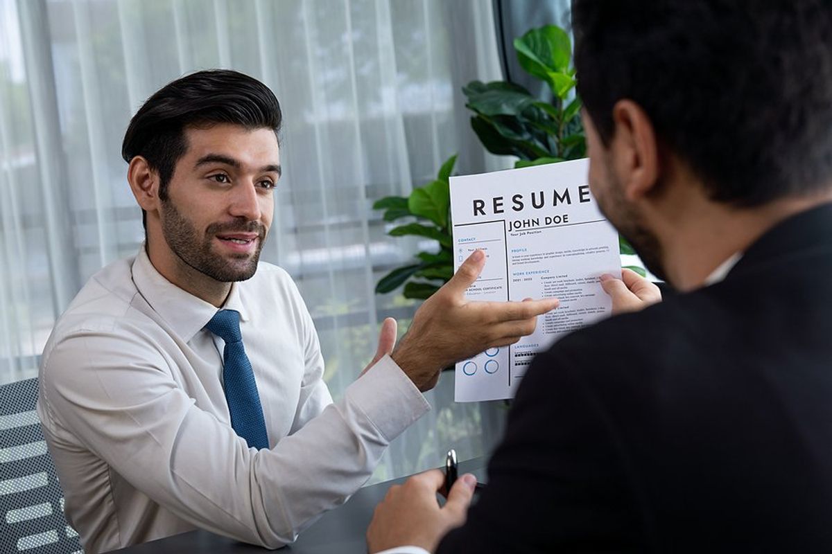 Man holds up his resume and answers the interview question, "How do you rate yourself?"
