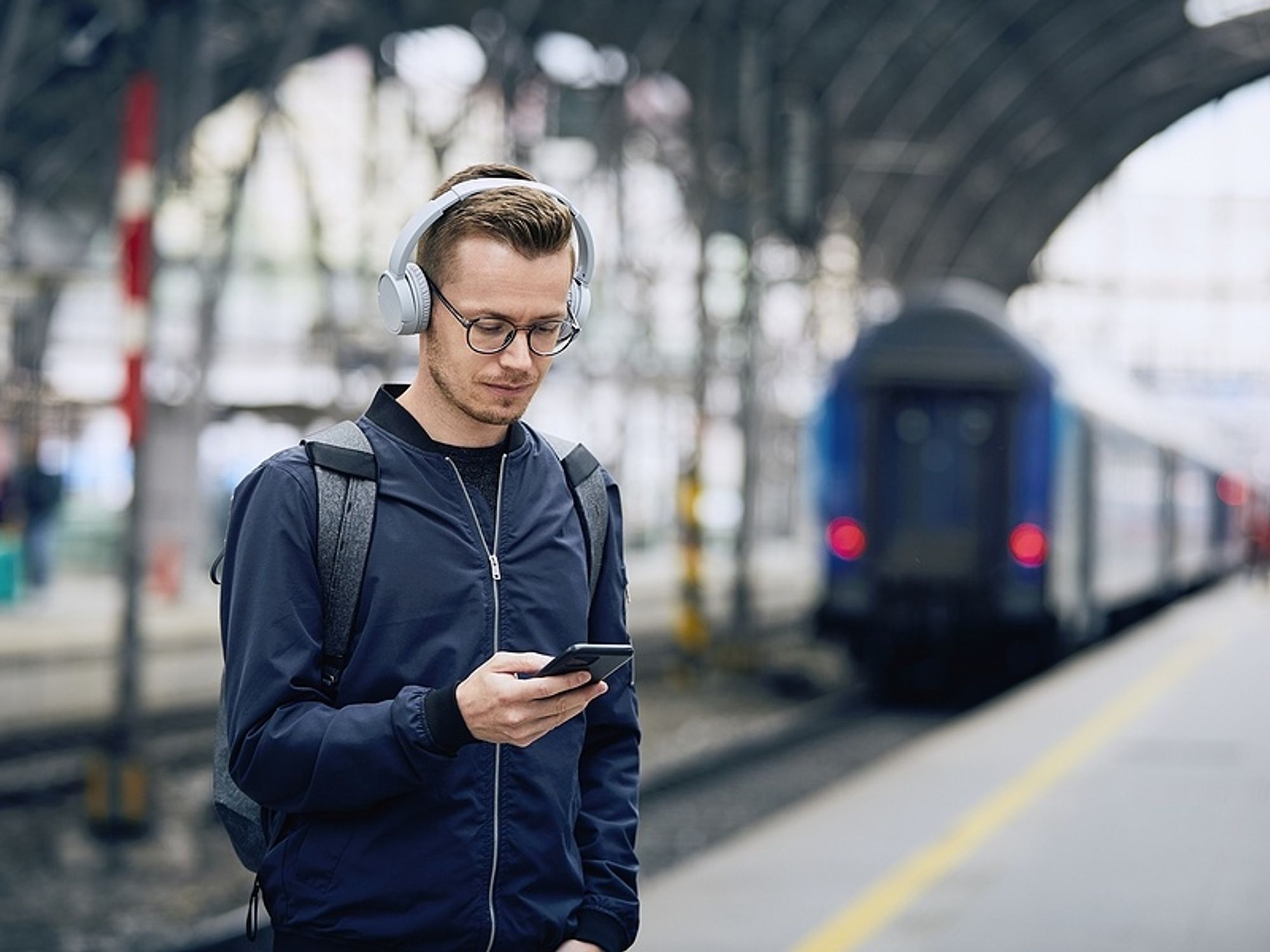 Man listens to uplifting podcast episodes while waiting for a train