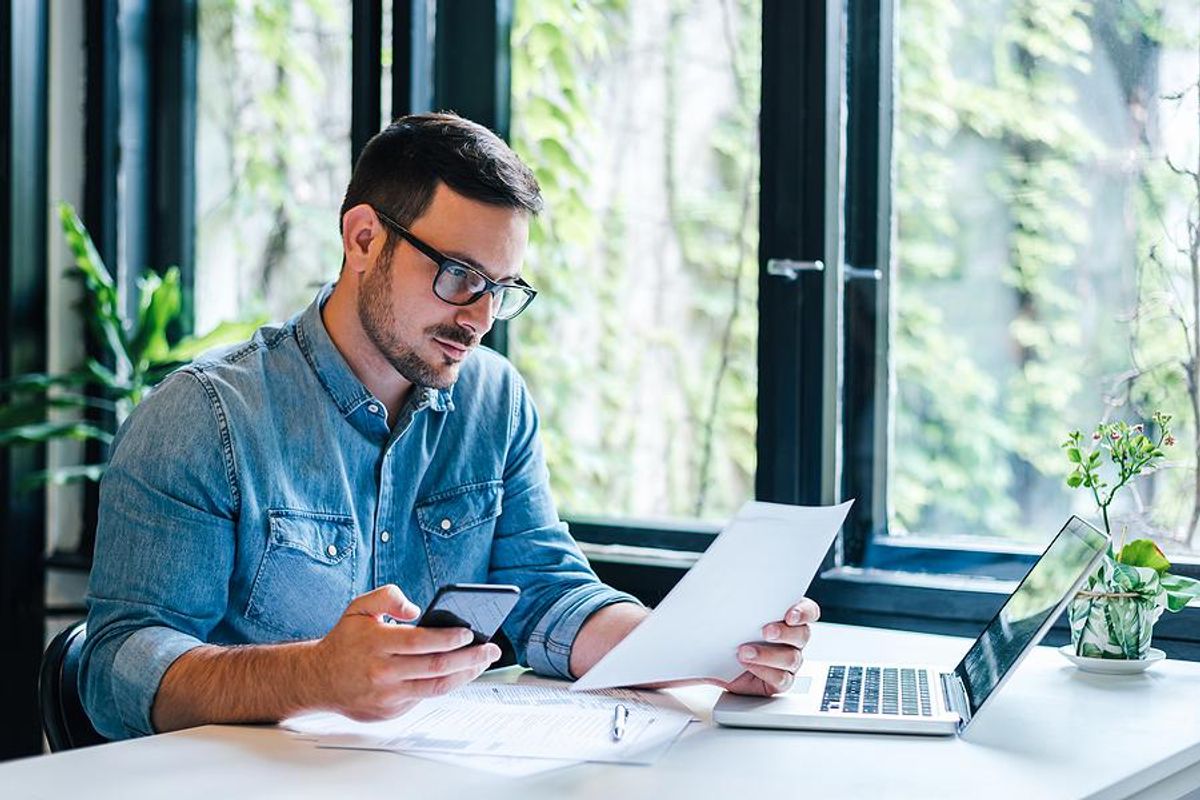 Man looks at his phone while holding his resume