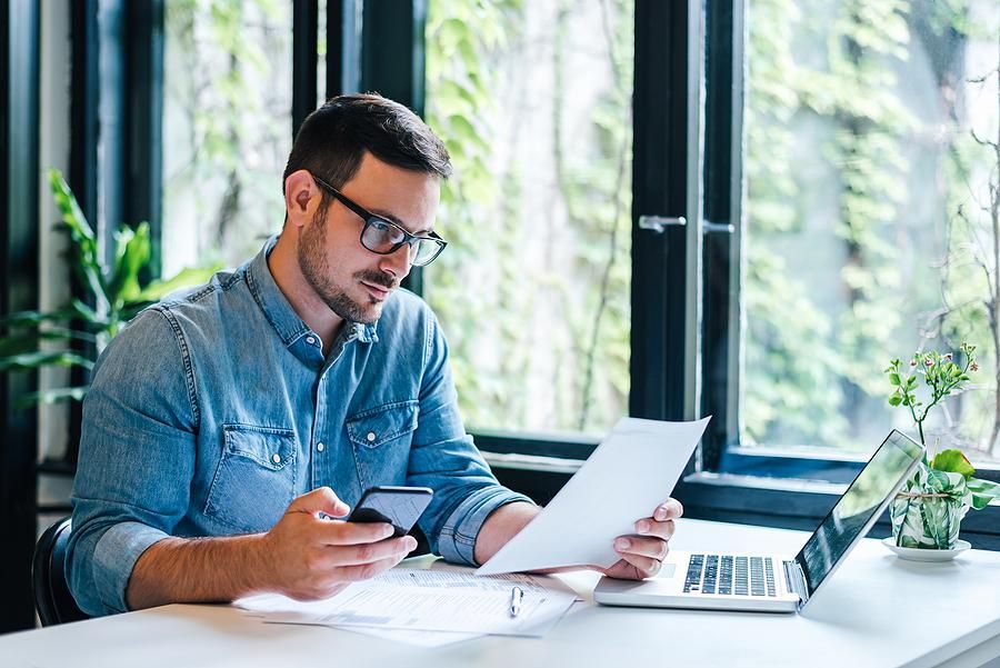 Man looks at his phone while holding his resume