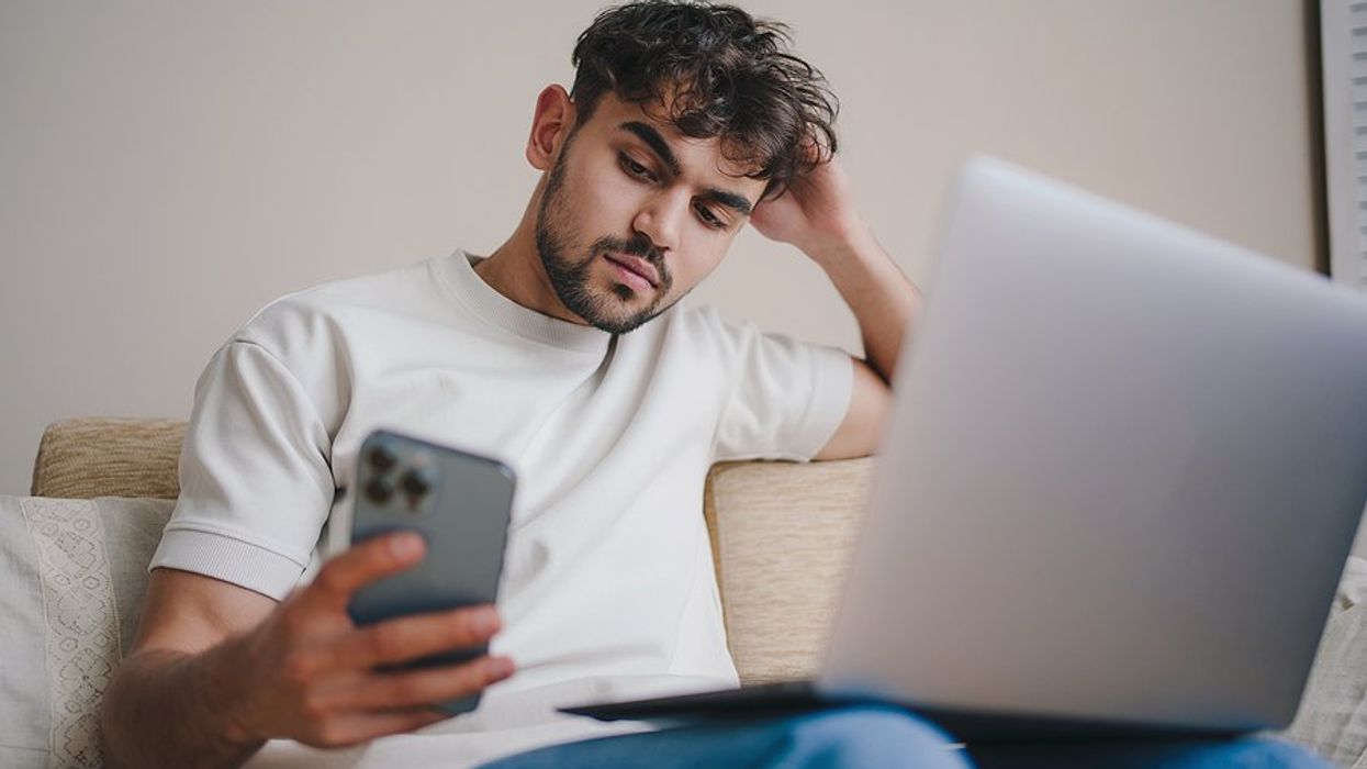 Man looks at his phone while working on his resume on his laptop