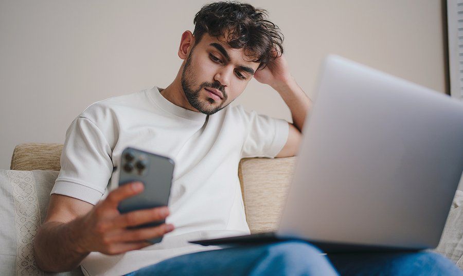 Man looks at his phone while working on his resume on his laptop