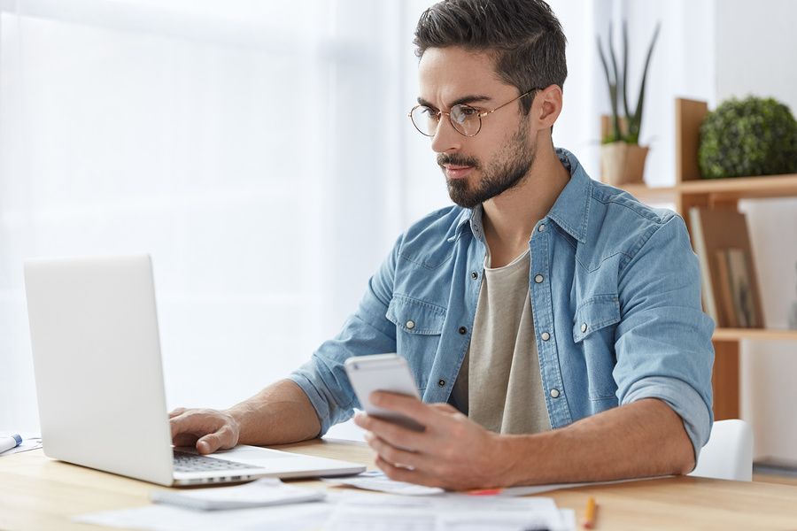 Man on laptop and phone following up with an employer after a job interview