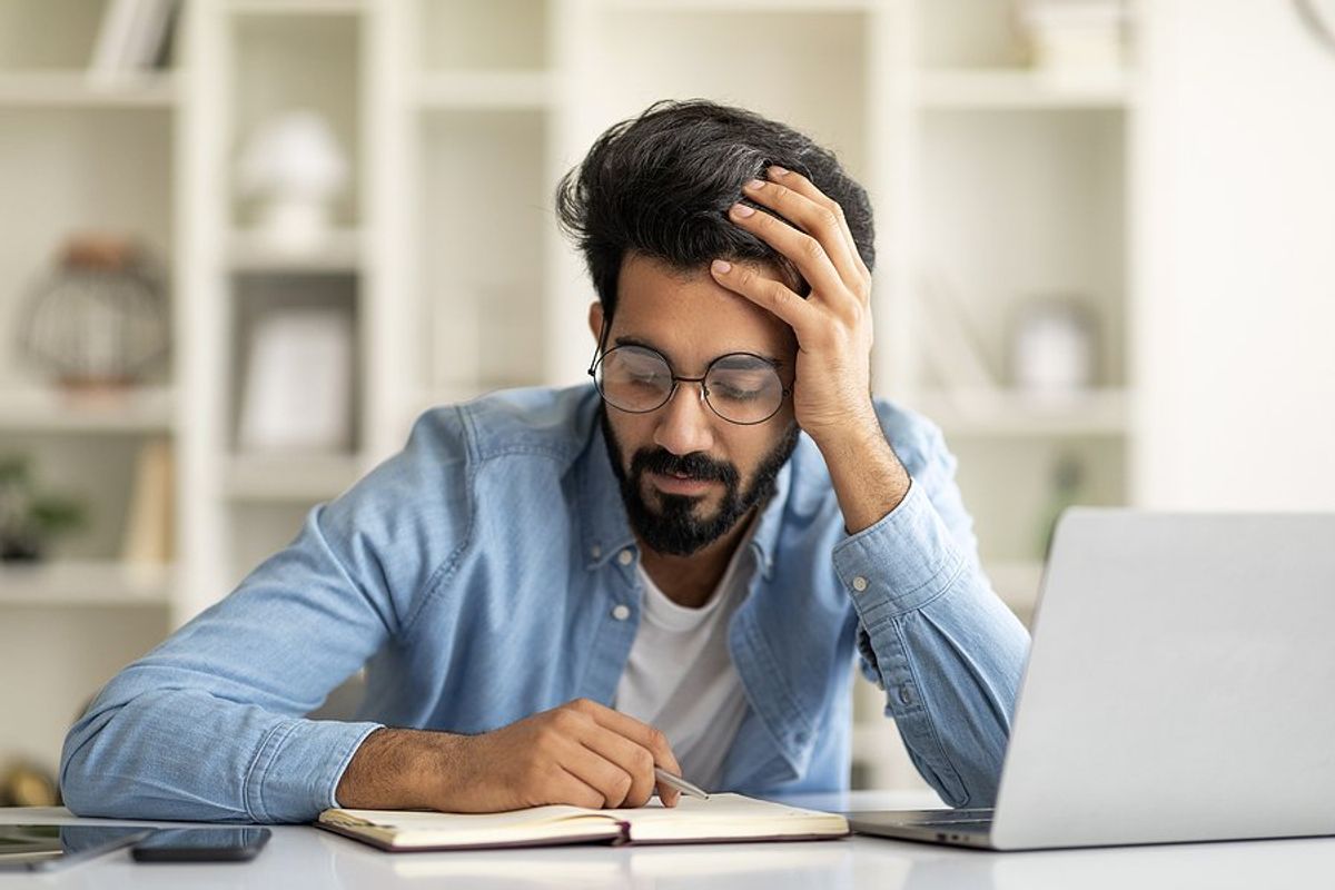 Man on laptop makes some cover letter mistakes and looks at his notes for guidance