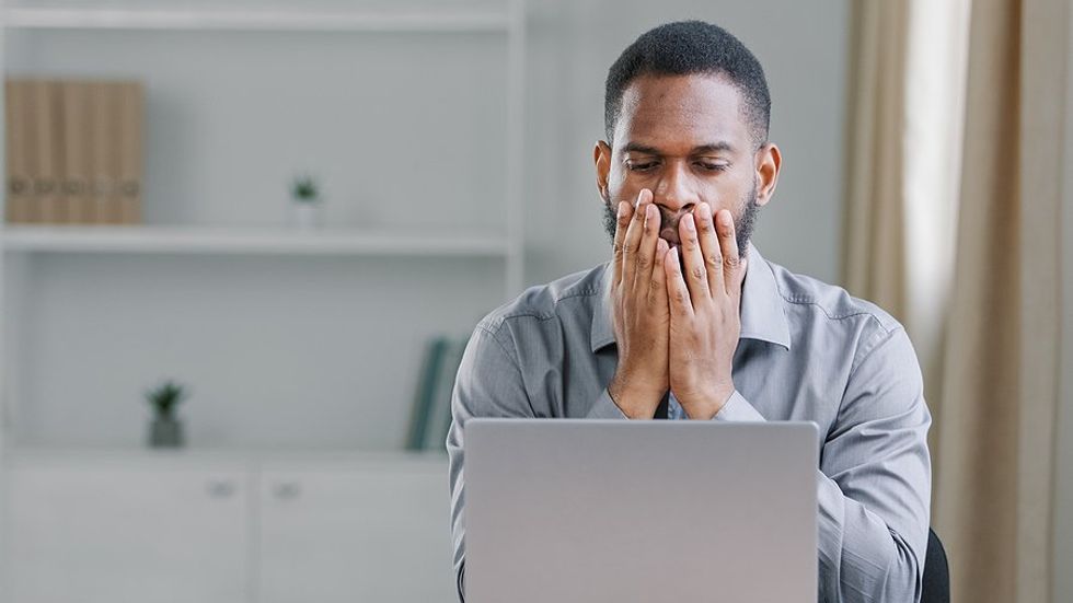 Man on laptop shocked, stressed about a failure at work