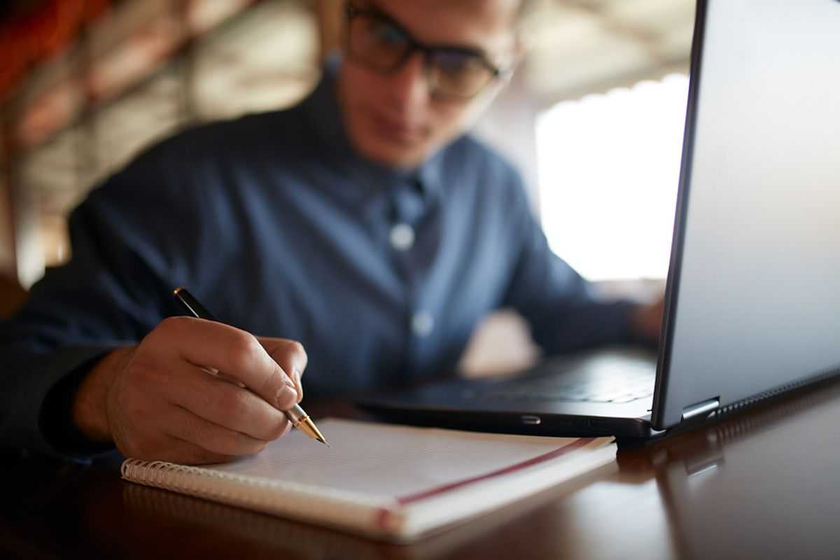 Man on laptop writes down his schedule for good time management