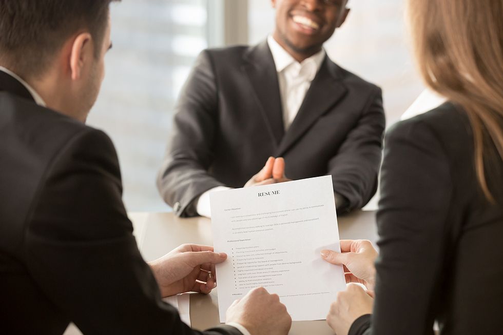 Man smiles while two hiring managers read his resume during a job interview