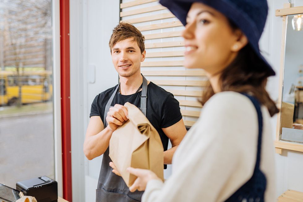 Man working in retail management hands a woman her bag