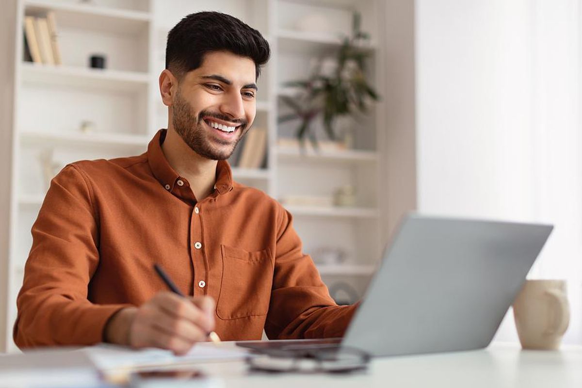 Man writes something down while working on laptop