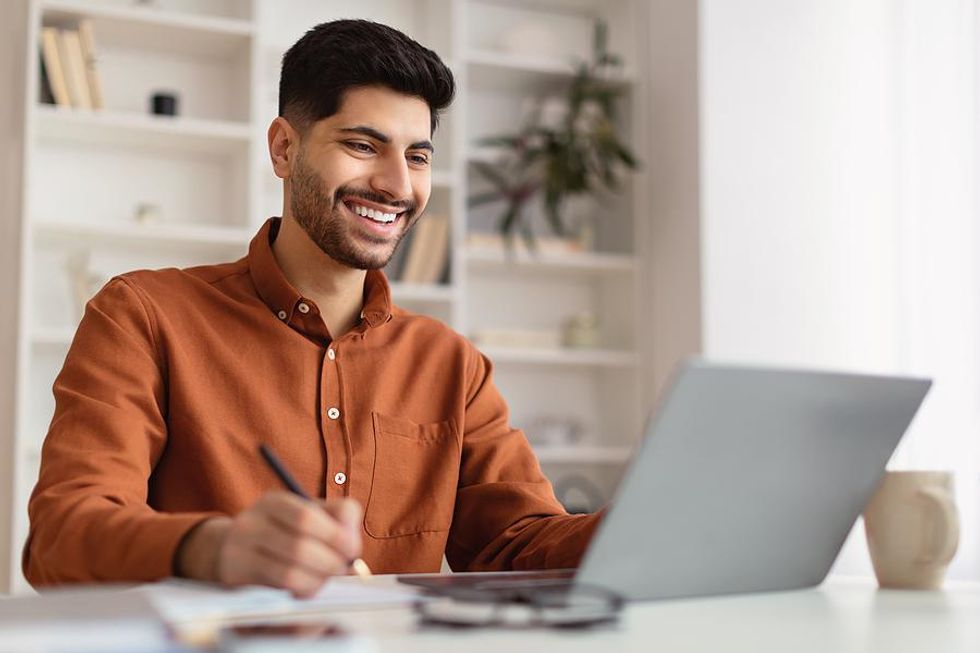 Man writes something down while working on laptop