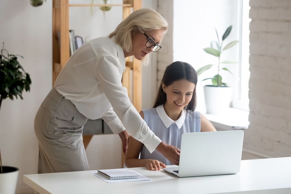 Manager shows an intern how to do something on her laptop