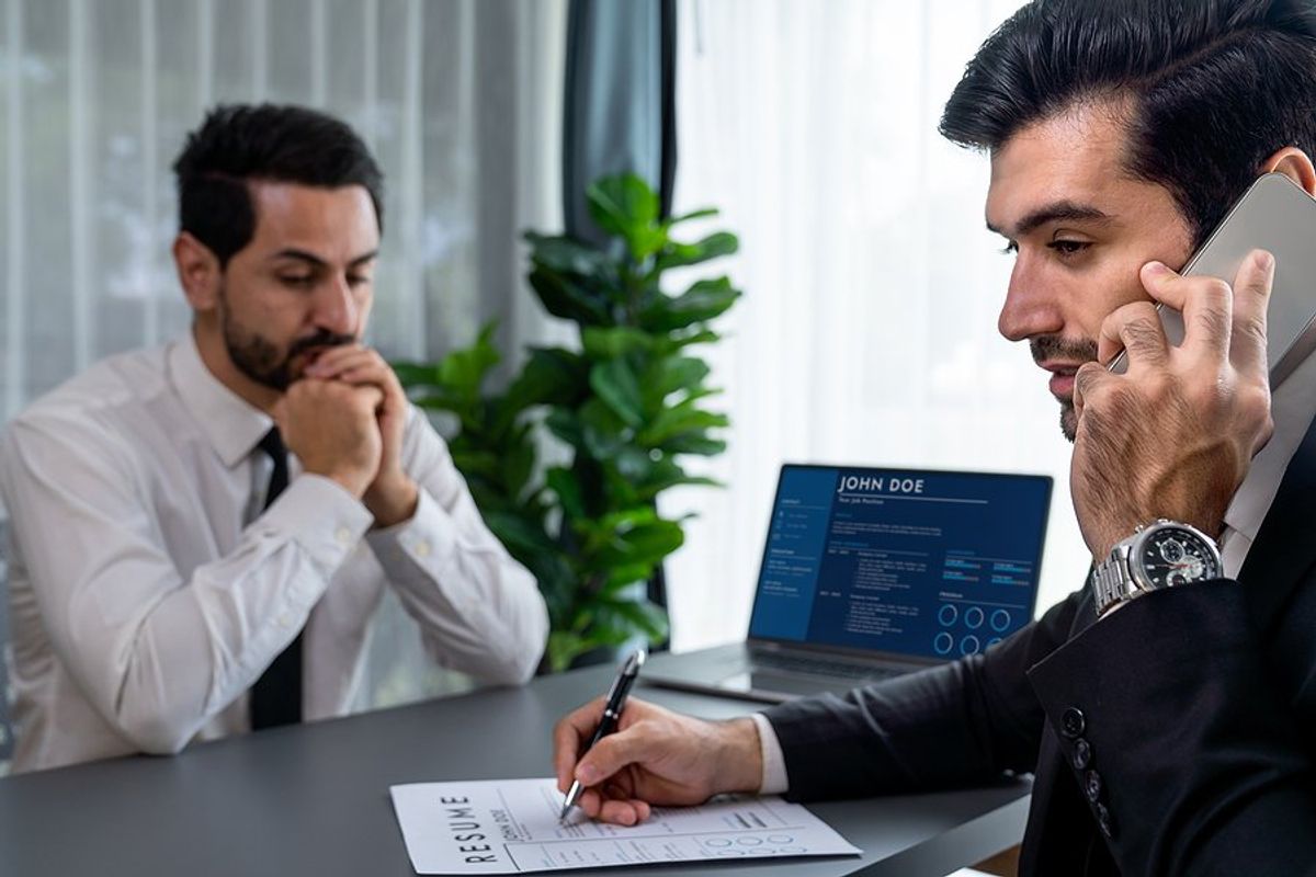 Nervous man in interview waits while the hiring manager talks on the phone