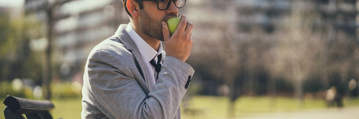 Professional man eating a fiber-rich apple as an afternoon snack at work