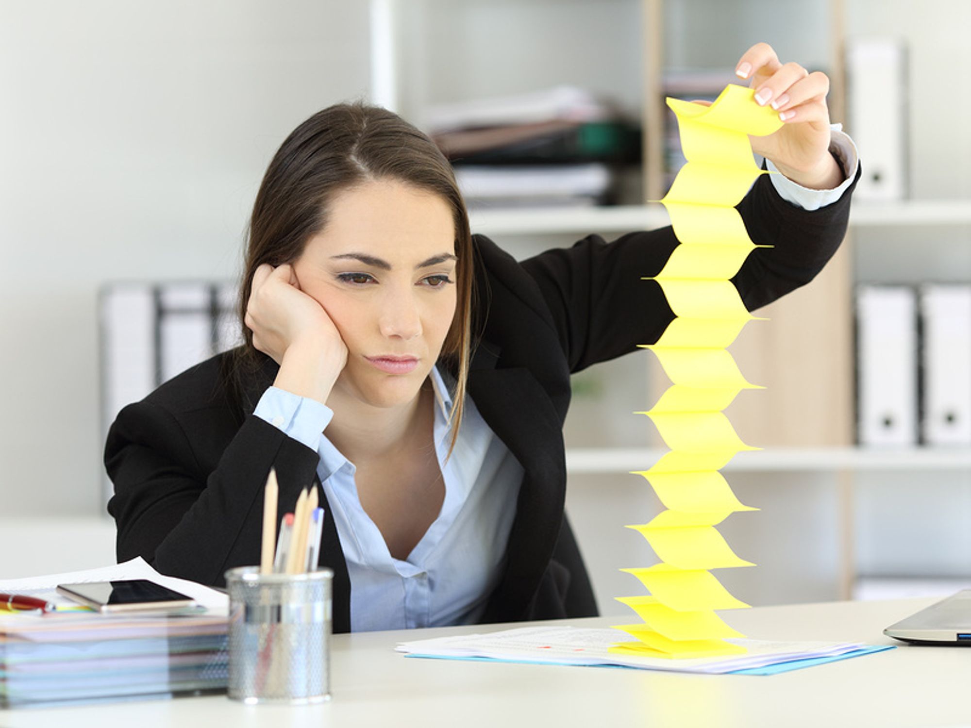 Professional woman feeling unmotivated at work and playing with sticky notes at her desk.