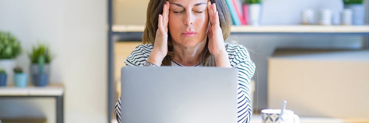 Professional woman sitting at table and working on computer, looking frustrated after receiving a work email with a passive aggressive phrase in it.