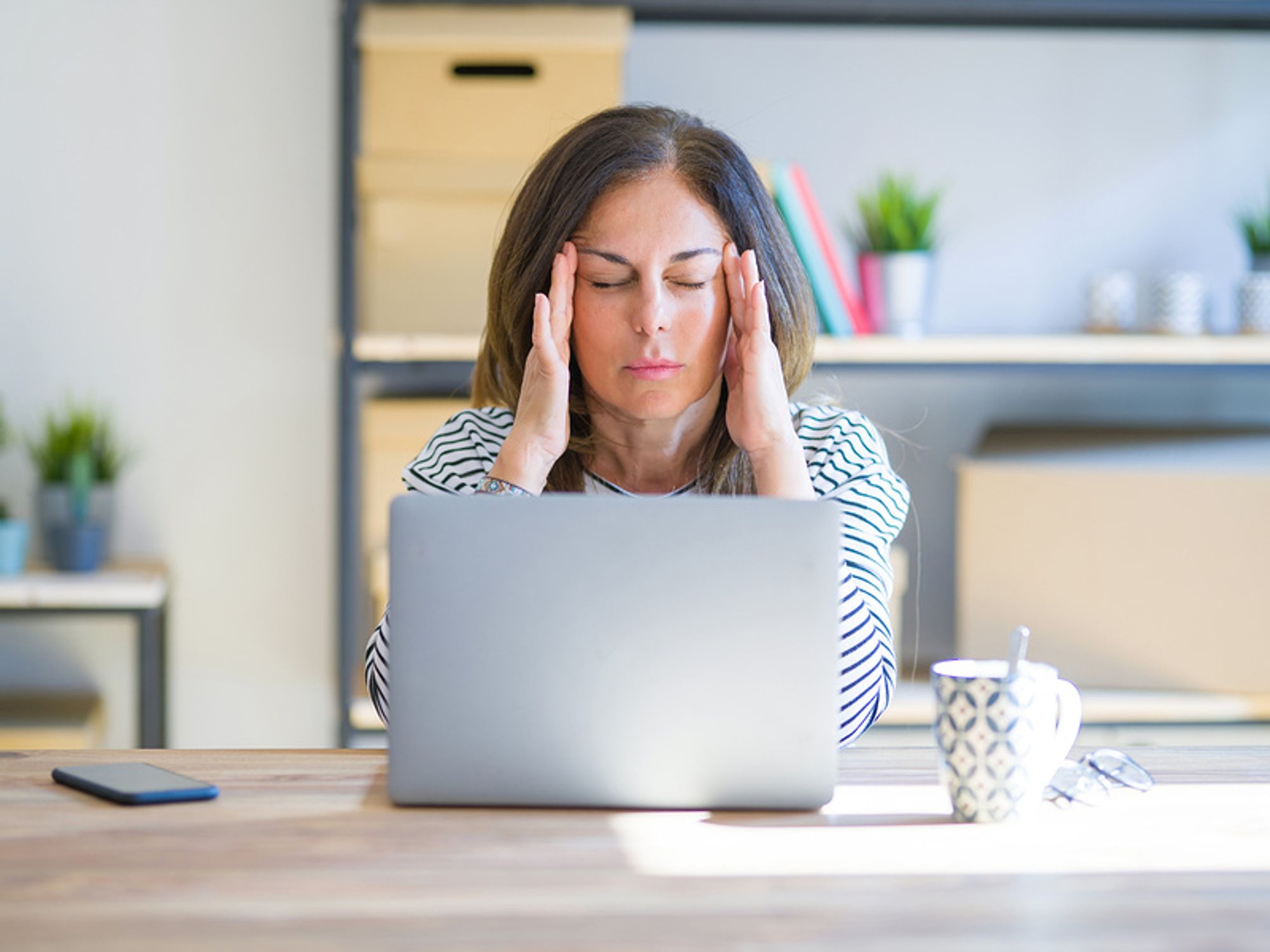 Professional woman sitting at table and working on computer, looking frustrated after receiving a work email with a passive aggressive phrase in it.