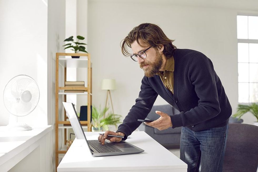 Un hombre serio en una computadora portátil sostiene su teléfono mientras rechaza una oferta de trabajo
