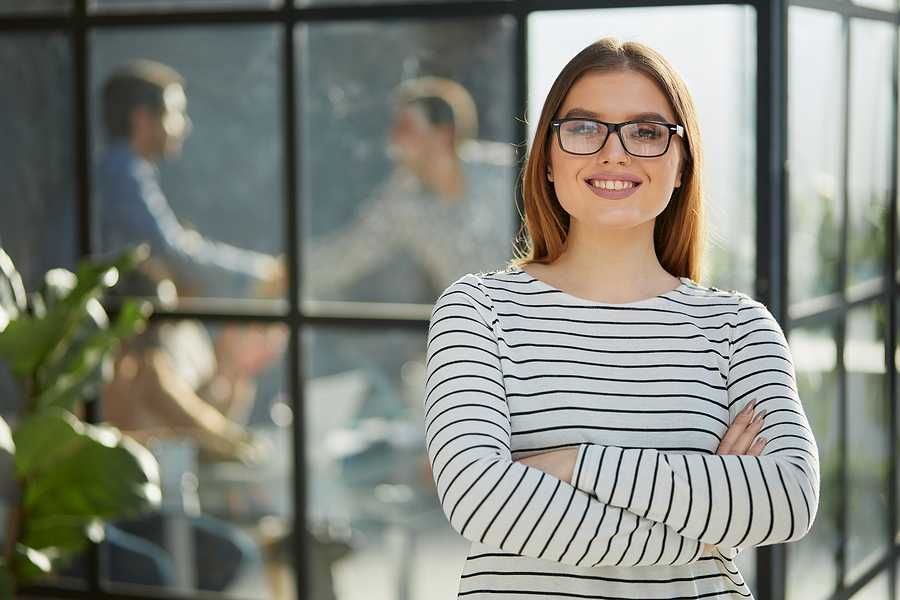 Smiling, professional woman stands with her arms crossed as she thinks about finding her purpose