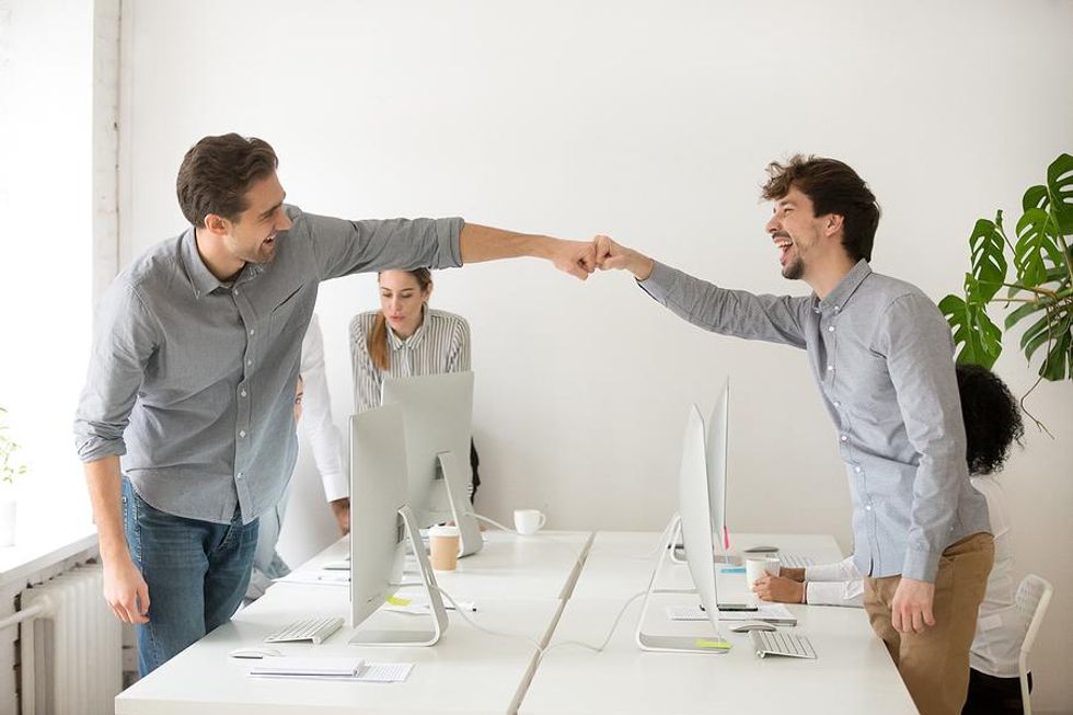 Two happy coworkers celebrate their office pool success with a fist bump