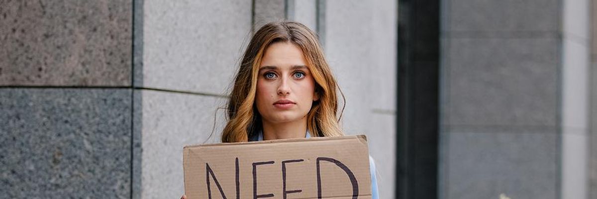 Unemployed woman holds a sign that says, "need work"