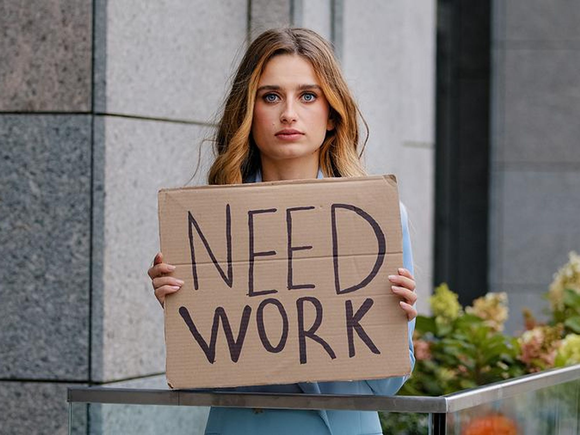 Unemployed woman holds a sign that says, "need work"
