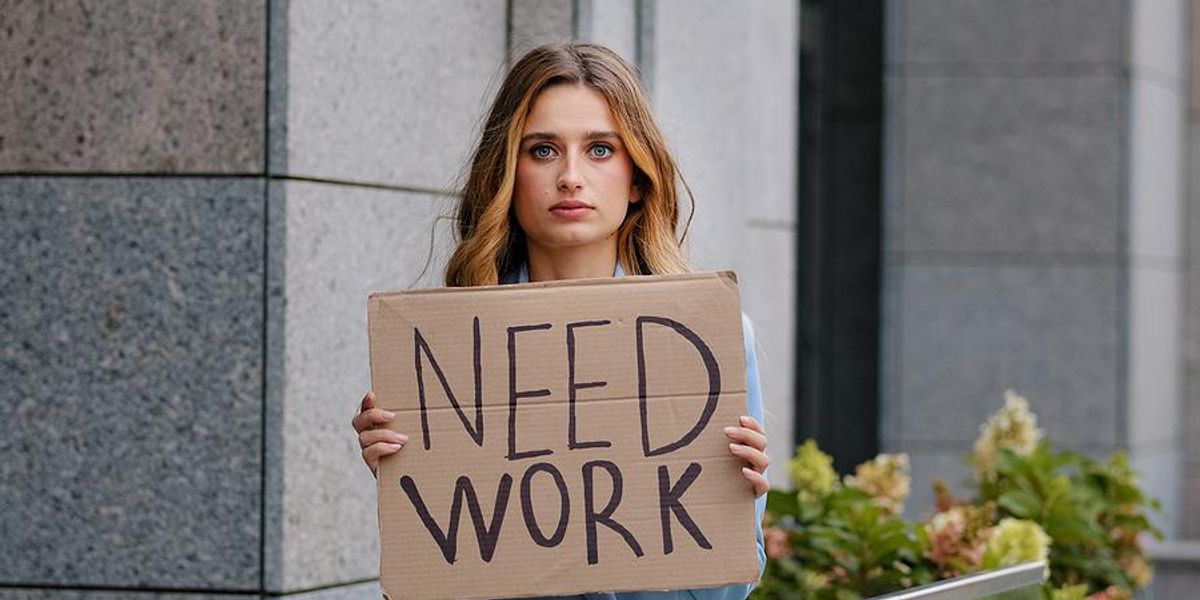 unemployed woman holds a sign that says need work